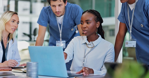 Doctors and staff discuss while gesturing to laptop.